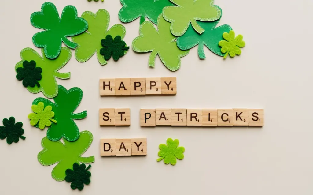 Scrabble Letter Tiles Saying Happy St. Patricks Day and Green Paper Clovers Scattered Around It